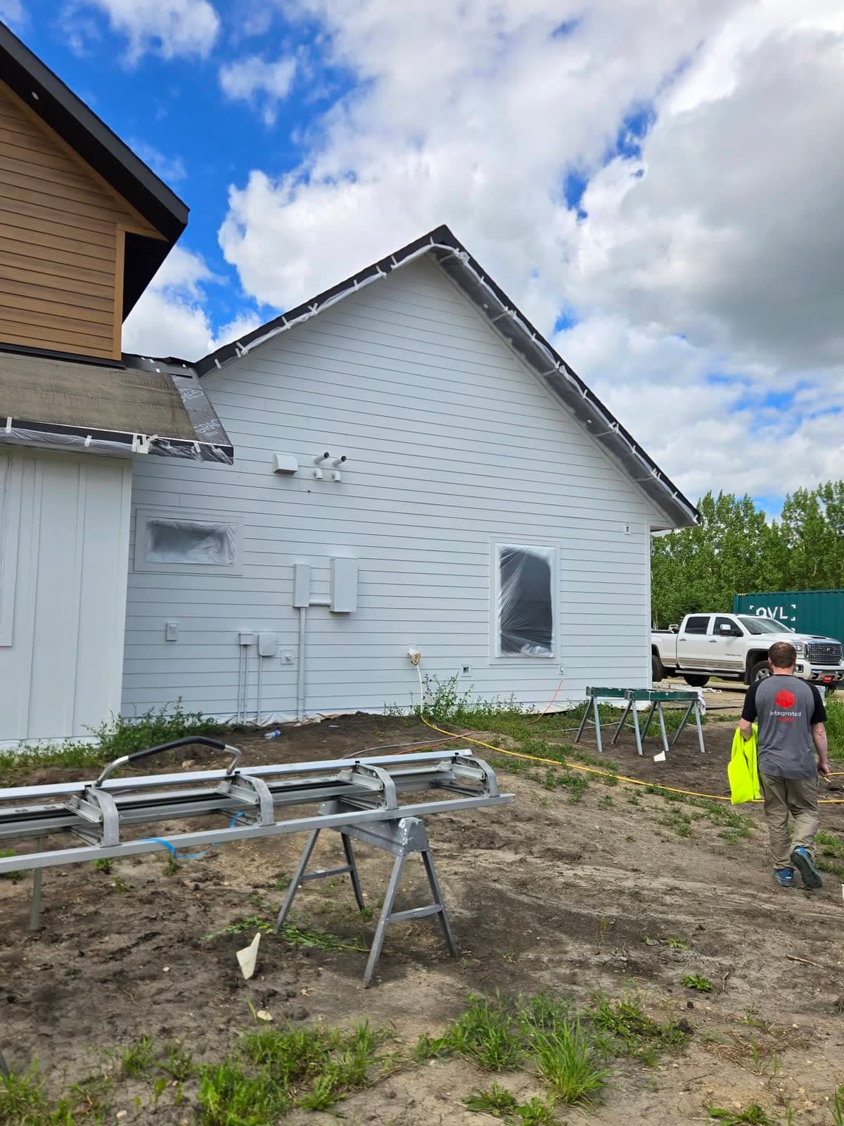 White gable end of a house mid-project, with staging and a work truck on the ground