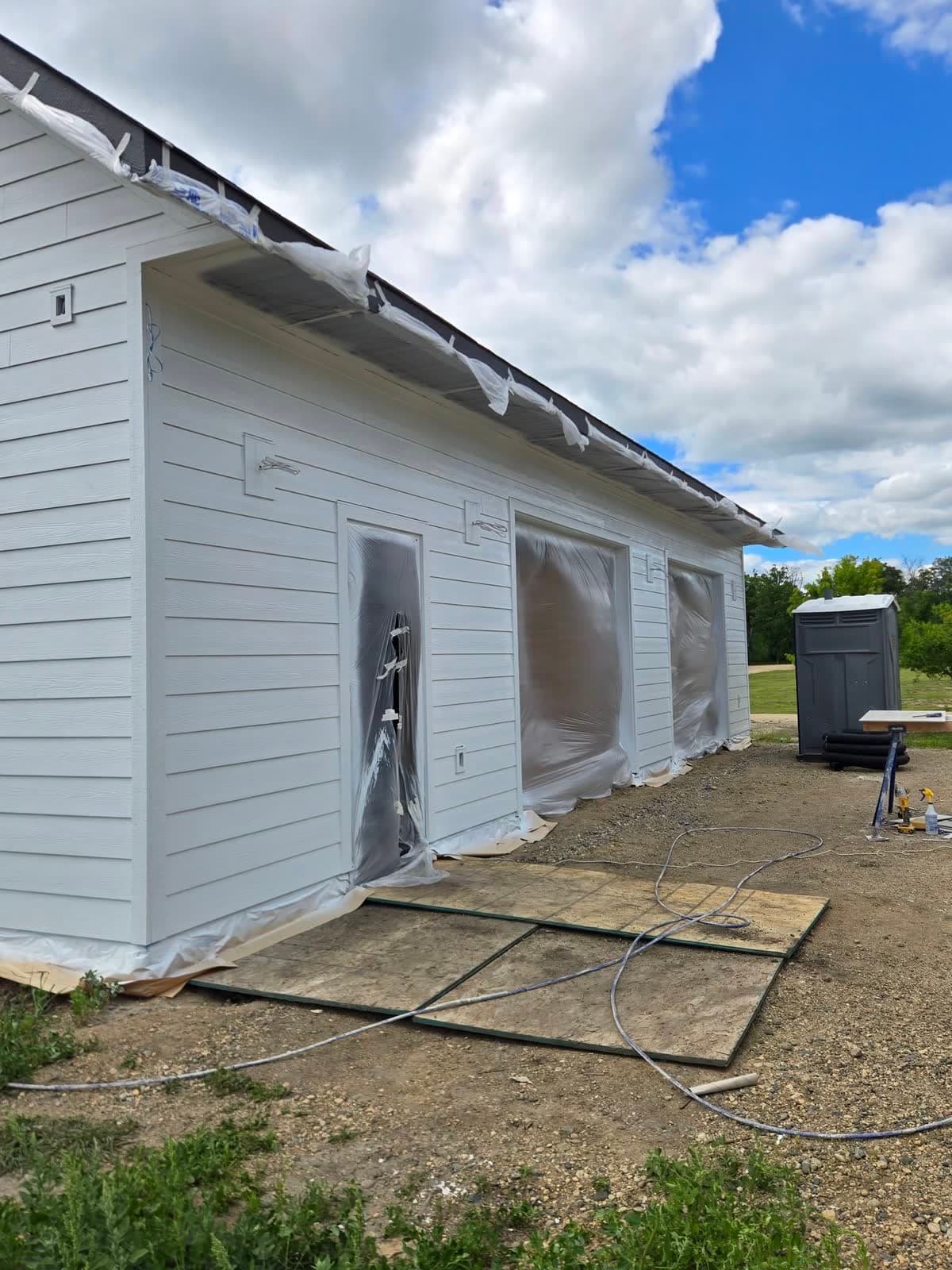 White lap siding on a house with the windows and openings masked off in plastic before painting